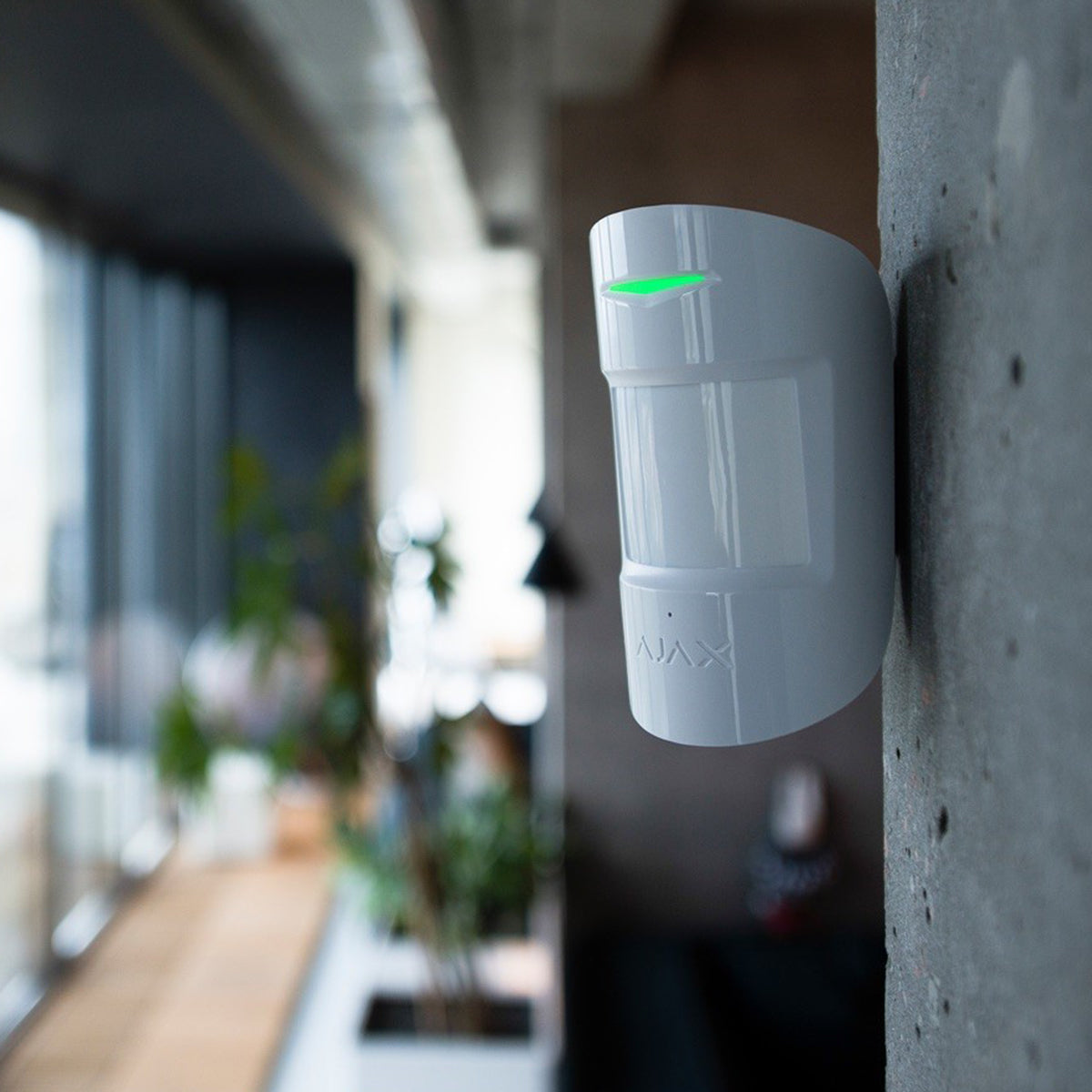 Ajax wireless indoor motion sensor mounted on a wall with a green indicator light.